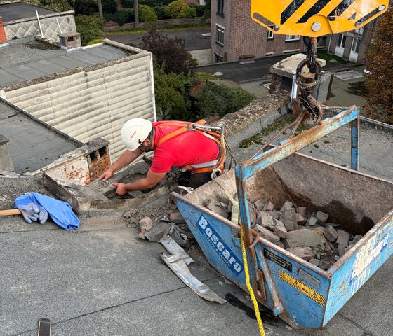 Ouvrier évacuant des gravats de toiture vers un conteneur levé par grue